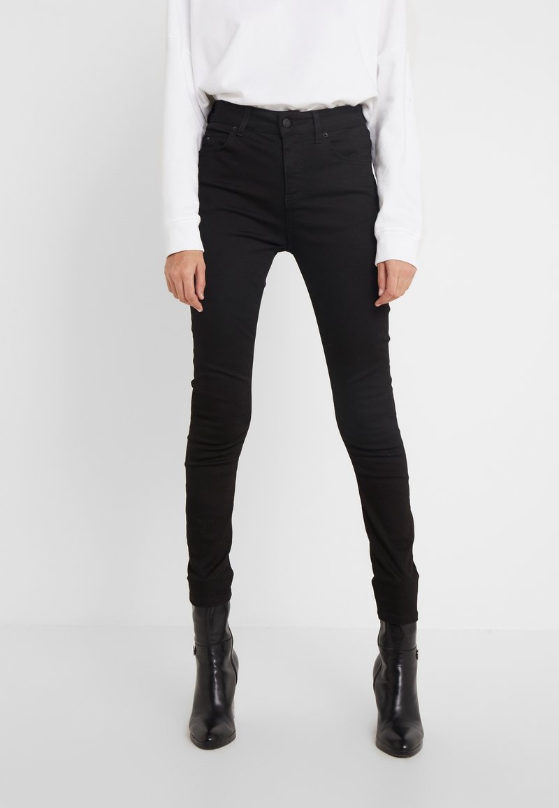 Jeans ajustados de tiro alto en color negro, fabricados en denim con una textura suave. Cuentan con un cierre de botón en la parte frontal y bolsillos traseros, combinados con botas negras.