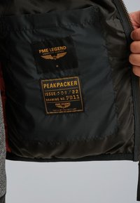 Unutarnji džep jakne s dvije crne i narančaste oznake, jedna s natpisom "PME Legend American Classic," a druga "Peakpacker Issue 508/22 Drawing No. PB11."