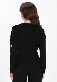 Czarny krótki sweter z cekinowymi akcentami na ramionach, dzianinową fakturą, długimi rękawami i dopasowanym pasem dla eleganckiego wyglądu.