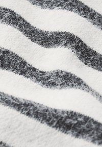 Černobílá pruhovaná látka s měkkou strukturou, obsahující vlnité linie. Povrch vykazuje jemné chmýří a detailní kontrast mezi barvami.