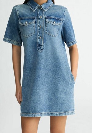 Vestido de mezclilla con mangas cortas, cuello con solapa, dos bolsillos en el pecho y cierre de botones. Presenta un lavado azul claro y un corte relajado.