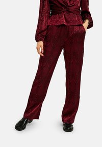 Bordové vzorované nohavice z hladkej tkaniny s dizajnom hadej kože. V kombinácii s čiernymi mokasínami pre kontrast.