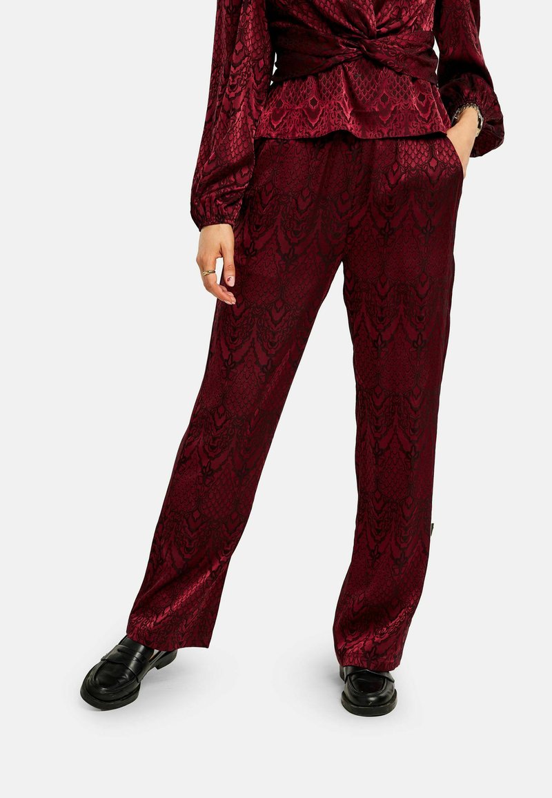 Bordové vzorované nohavice z hladkej tkaniny s dizajnom hadej kože. V kombinácii s čiernymi mokasínami pre kontrast.