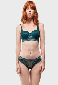 Bralette teal con ferretto e dettagli in rete; perizoma abbinato con motivi geometrici; entrambi presentano bordo in pizzo e spalline regolabili.