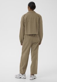 Chaqueta beige cortada con un cuello abotonado, combinada con pantalones beige holgados. Llevada con zapatillas deportivas grises y blancas.