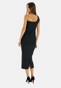 Vestido midi negro de un solo hombro hecho de un material suave, con cierre de cremallera en la parte trasera y una abertura lateral. Estilizado con tacones altos negros.