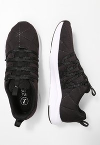 Svarta sportskor med quiltad textur, elastiska snören och en vit gummisula. Inkluderar logotyp på tungan och på hälen.