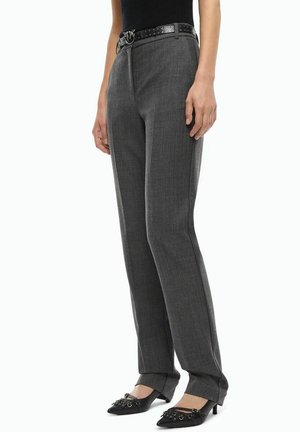 Mujer con pantalones grises de corte recto, cinturón negro con tachuelas y tacones negros de punta con pequeños detalles metálicos.