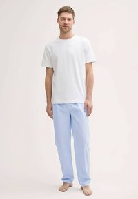 T-shirt en coton blanc associé à un pantalon de pyjama bleu clair à rayures, avec une coupe décontractée et une texture de tissu douce, porté pieds nus.