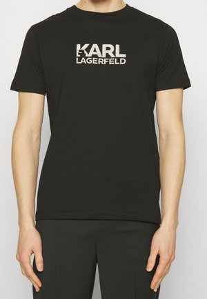 Hombre que lleva una camiseta negra ajustada con "KARL LAGERFELD" impreso en letras blancas en negrita en el pecho.