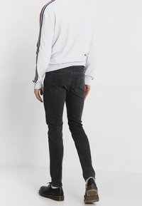 Jeans ajustados de color gris oscuro con una textura suave y bolsillos traseros, combinados con un sudadera gris clara que presenta franjas laterales en rojo y azul.