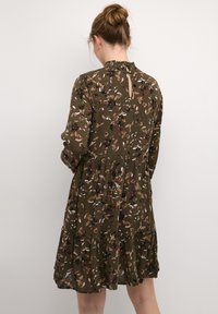 Robe vert olive avec un motif floral, décolleté froncé, manches longues et jupe à volants. Comprend une ouverture en forme de trou de serrure au dos.