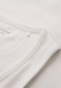 Tessuto bianco a righe con scollatura a barca e dettagli di rigatura stretta. Etichetta visibile vicino al colletto, che indica la taglia M. Superficie texture.