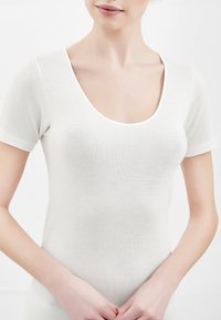 Top corto bianco aderente con scollatura a girocollo, realizzato in materiale morbido e leggero; texture liscia senza motivi o decorazioni visibili.