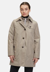 Beige vattentät jacka med knäppning, två stora sidofickor och klassisk krage, med en mjuk och lätt textur.