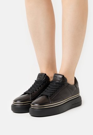 Black leather sneakers with textured surface, featuring black laces, a gold accent line, and a thick black sole.