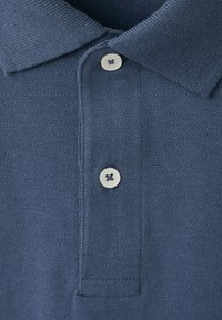 Col du polo texturé bleu avec deux boutons blancs fixés sur la patte de boutonnage.