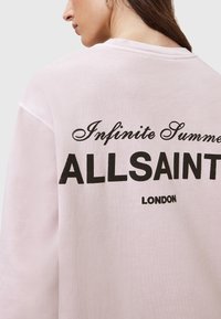 Svetloružový mikina vyrobená z mäkkého materiálu, s nápisom "Infinite Summer" v písanom písme a "ALLSAINTS LONDON" v tučnom čiernom písme na zadnej strane.