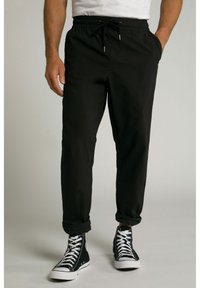 Joggers negros con cintura elástica y cordón, bolsillos laterales, piernas ajustadas y puños enrollados. Combinados con zapatillas negras de caña alta.