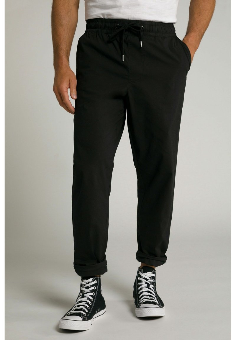 Joggers negros con cintura elástica y cordón, bolsillos laterales, piernas ajustadas y puños enrollados. Combinados con zapatillas negras de caña alta.
