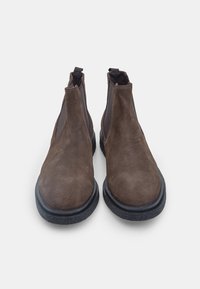 Stivali ankle in suede marrone con pannelli laterali elasticizzati, punte arrotondate e suole in gomma nera testurizzata. Doppi tasselli per una facile calzata.