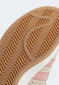 Sneaker sole with a textured, wavy pattern in tan rubber, featuring light pink and beige accents on the side and a white rubber base.