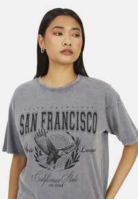 T-shirt gris à manches courtes avec l'inscription "SAN FRANCISCO", comportant un graphique d'aigle et une laurier décorative, en coton, coupe décontractée.
