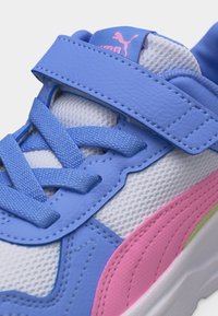 Κοντινή λήψη μπλε και ροζ αθλητικού παπουτσιού με μπλε κορδόνια και λουράκι πάνω από λευκό πλεκτό ύφασμα, με το λογότυπο της Puma στη μπλε γλώσσα.