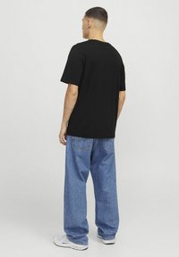Sort bomulds T-shirt med korte ærmer, parret med løstsiddende blå denimjeans. Modellen har hvide sneakers på.