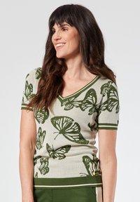 Top de punto con estampado de mariposas en verde, con escote en V, mangas cortas y ribete verde de contraste en los bordes. Tejido texturizado.