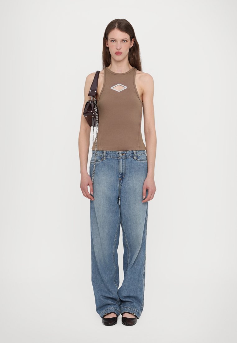 Haut sans manches marron clair avec une découpe en forme de diamant, associé à un jean en denim bleu ample. Les accessoires comprennent un petit sac sombre avec une chaîne.