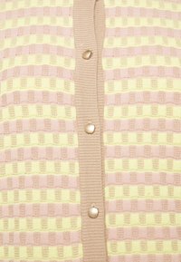 Cardigan s texturovaným vzorem v růžové a žluté barvě, s béžovým žebrovaným límcem a pěti kulatými knoflíky na přední straně.