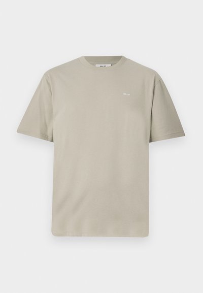 Light taupe cotton t-shirt with short sleeves, round neckline, and a small printed logo on the left chest area. Soft, smooth texture.