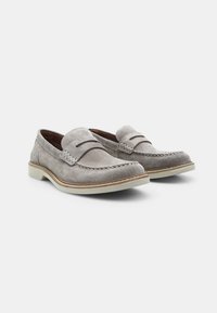 Mocasini gri din suede, cu accente cusute duale, vârf rotund și o talpă albă contrastantă. Prezintă un design simplu de tip slip-on.