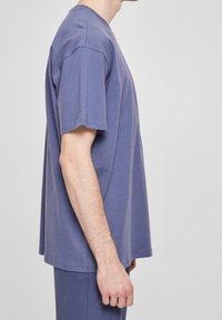 Vista laterale di una persona che indossa una maglietta blu a maniche corte e pantaloni blu abbinati, su uno sfondo semplice.