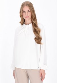 Camicia bianca con maniche lunghe e dettaglio a fiocco al collo. Tessuto liscio e leggero, vestibilità comoda e design minimalista.