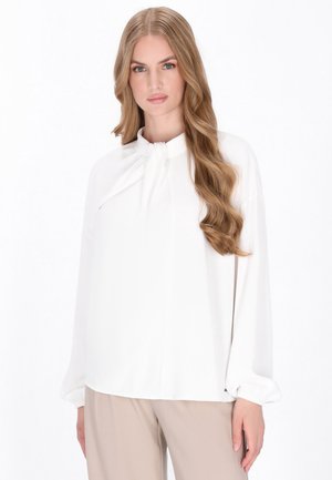 Weißes Bluse mit langen Ärmeln und einer Schleifenbindung am Hals. Glattes, leichtes Material, lockere Passform und ein minimalistisches Design.