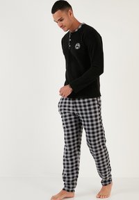 Camisa negra de manga larga con cuello de cuadro y logotipo; combinada con pantalones de pijama de cuadros grises y negros. Tejido suave con corte relajado.