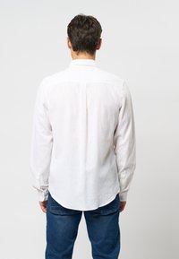 Valkoinen pitkähiha paita, kevyt kangas, kaareva helma, napilliset hihansuut ja klassinen kaulus. Yhdistetty farkkuihin.