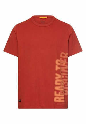 T-shirt à manches courtes couleur rouille avec col rond et texte vertical délavé "PRÊT À DÉCOUVRIR" sur le côté droit près de l'ourlet.