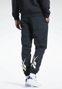 Schwarze sportliche Jogginghosen mit schmalem Schnitt, ausgestattet mit weißen Akzentstreifen an den Unterschenkeln und einem elastischen Bund. Getragen mit weißen Turnschuhen.
