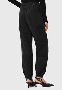 Zwarte cargobroek met een elastische tailleband, afgeknipte enkels en een patchzak. De stof heeft een lichte textuur, wat een casual uitstraling geeft.