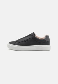 Zapatilla negra de cuero tipo slip-on con suela de goma blanca, con detalles de costuras laterales y un diseño superior liso para mayor comodidad.