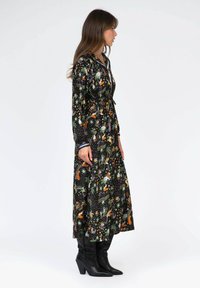 Robe noire avec un imprimé floral et animal, manches longues, taille à cordon, silhouette fluide, associée à des bottes noires à talons.