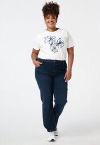 Witte t-shirt met marineblauwe bloemachtige lijntekening, gecombineerd met donkerblauwe spijkerbroek. Inclusief zakken en een ontspannen pasvorm. Gemaakt met witte sneakers.