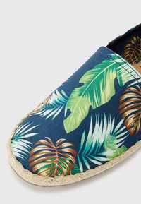 Espadrila odjeća s tamnoplavim materijalom koji ima uzorke tropskog lišća u zelenoj i smeđoj boji, šivani rub i đon od jute.