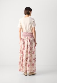 Cream t-shirt paired with a long, floral printed skirt featuring a smocked waist and pink accents, worn with beige shoes.