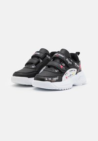 Zapatillas deportivas negras con suelas blancas, que cuentan con correas de Velcro, detalles perforados y texto y gráficos coloridos en los laterales.