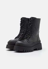 Black leather ankle boots with a textured finish, featuring a lace-up front, a chunky platform sole, and a side zipper detail.