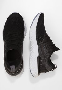 Zapatillas deportivas negras con una parte superior de punto transpirable, acentos negros texturizados y una suela blanca con amortiguación. Incluyen cordones planos y un branding mínimo.